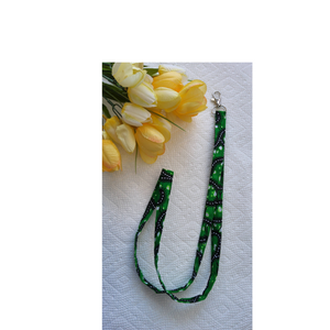 Green lanyard with black pattern on a white surface with yellow tulips.